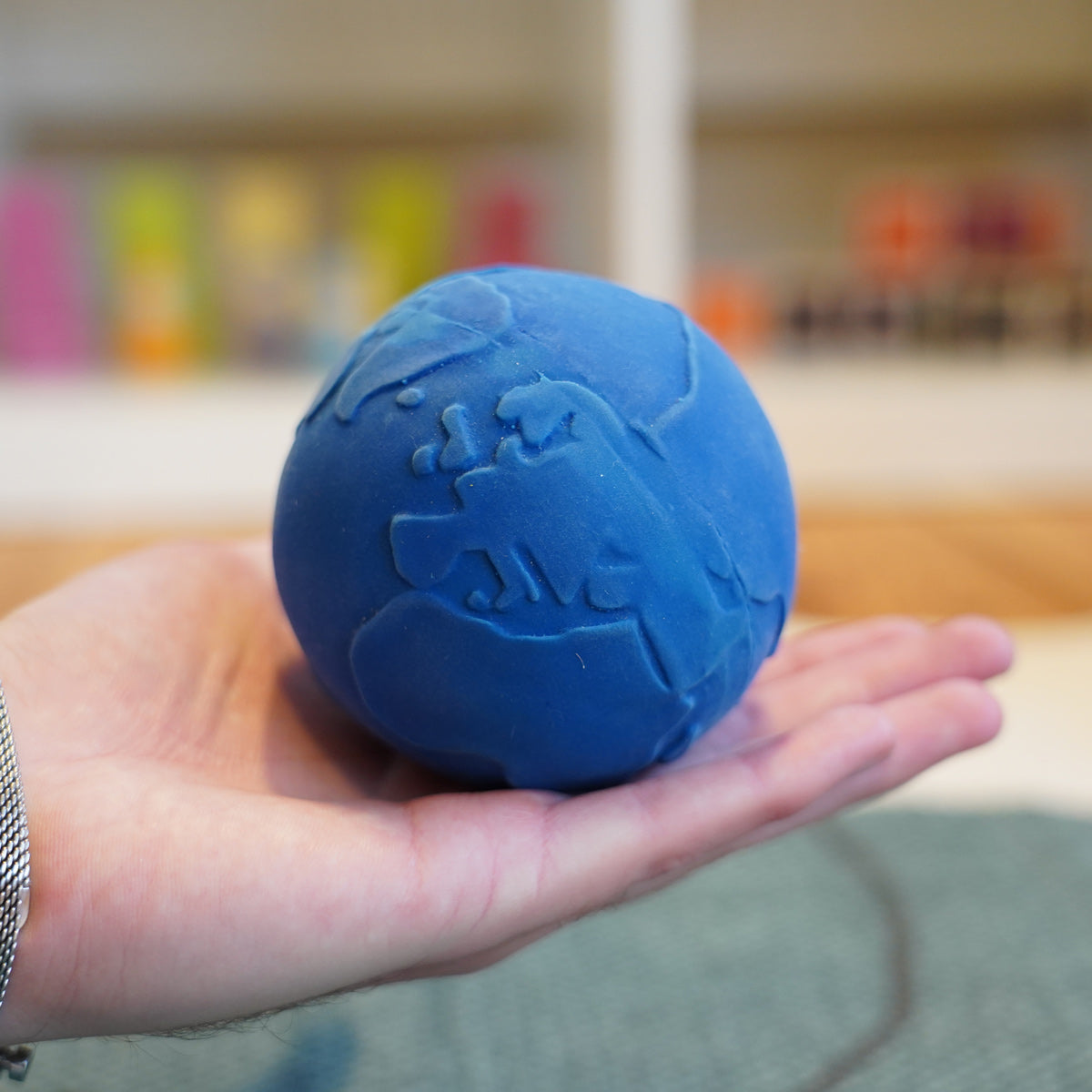 Close up of a hand holding the Lanco blue natural rubber globe ball in front of a blurred background