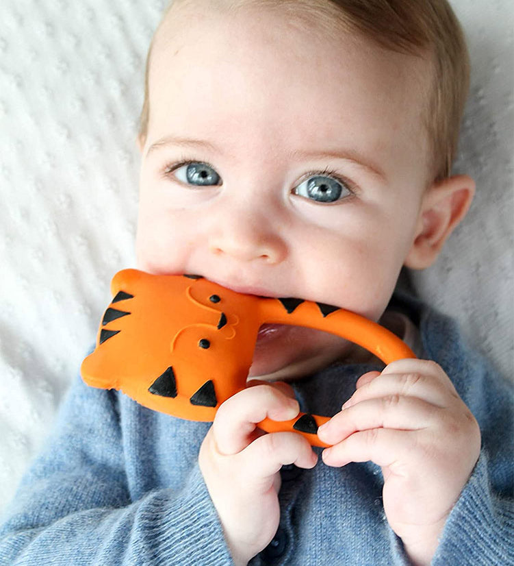 A baby holding and chewing on the Lanco Nalu the Tiger Teether