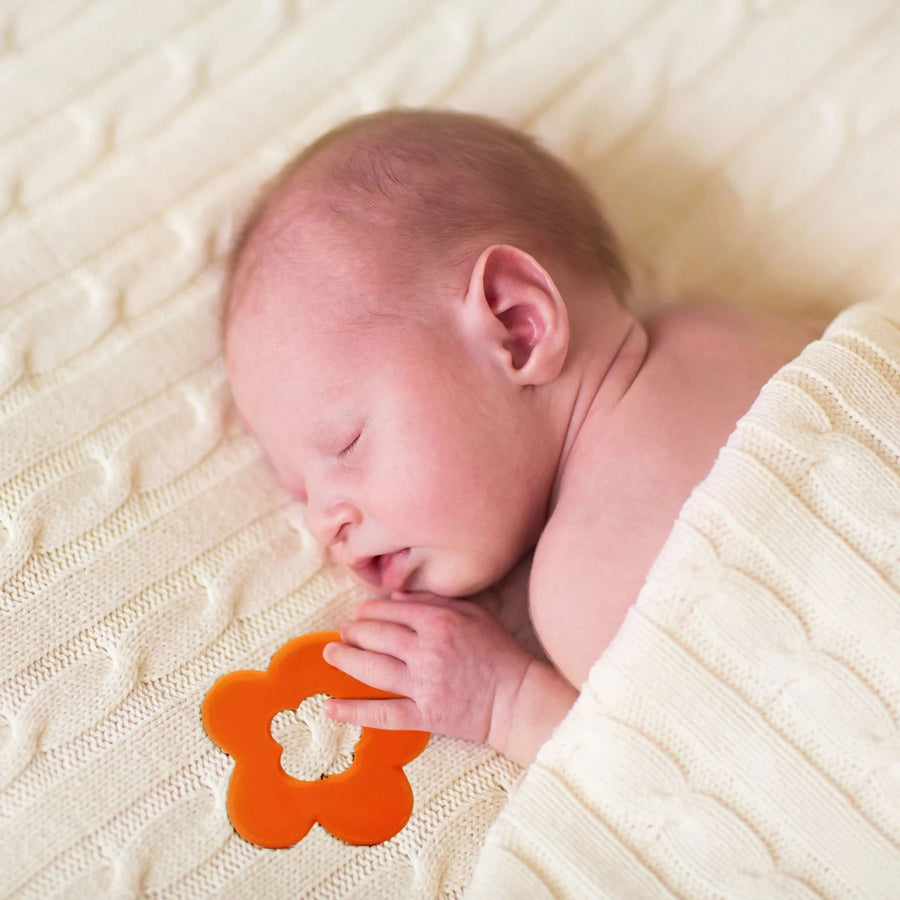 baby sleeping clutching onto the orange flower shaped teething toy by Lanco