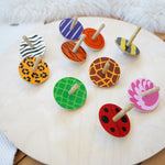 A group of the Lanka Kade animal wooden spinning tops on a Wobbel 360 wooden balance board on a wooden floor. Features a zebra, leopard, tiger, flamingo, giraffe, snail, beetle and bumblebee spinning top.