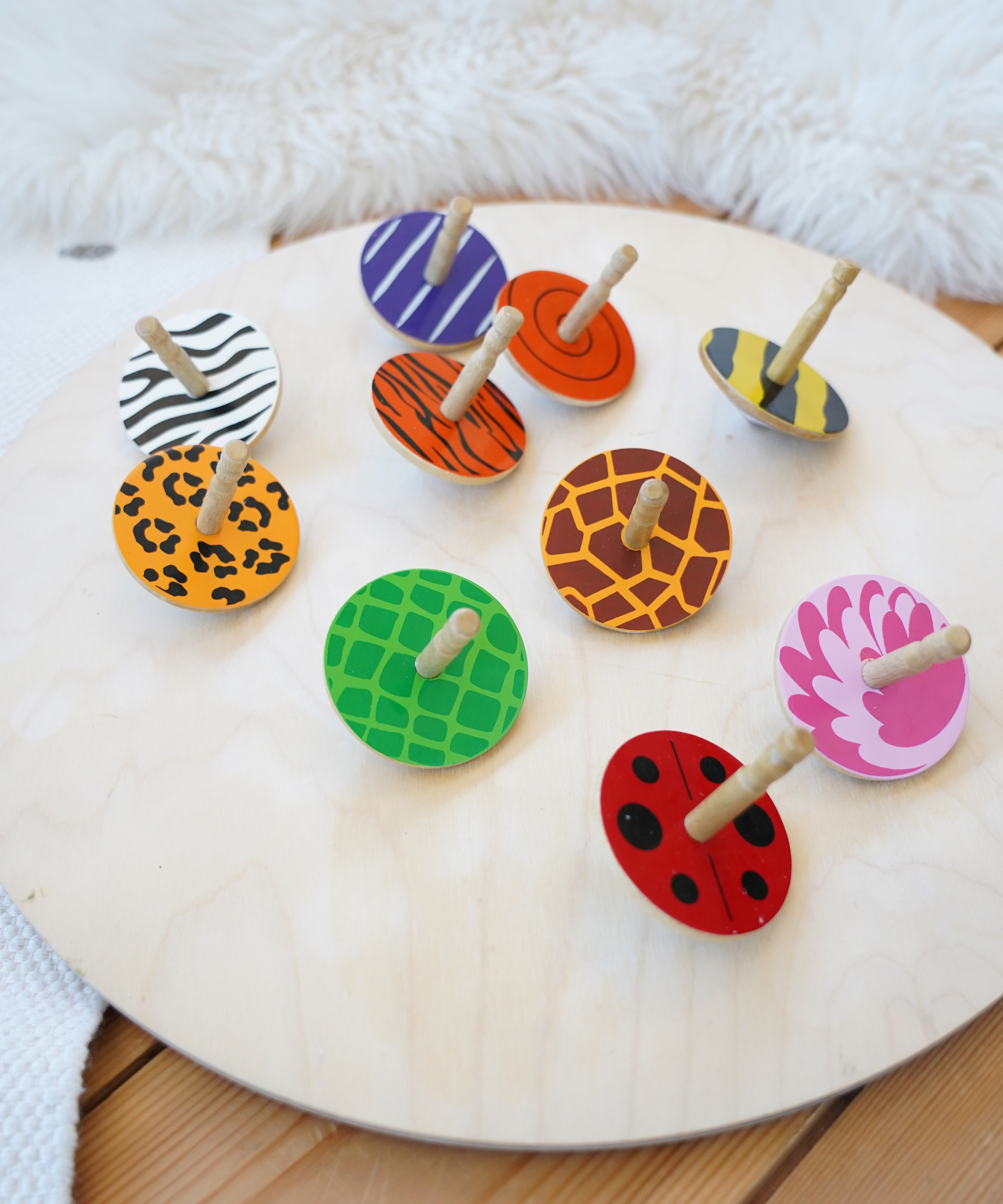 A group of the Lanka Kade animal wooden spinning tops on a Wobbel 360 wooden balance board on a wooden floor. Features a zebra, leopard, tiger, flamingo, giraffe, snail, beetle and bumblebee spinning top.