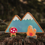 Close up of the Lanka Kade dan y ser campfire toy next to the Babipur moel mountains and toadstool on a wooden log