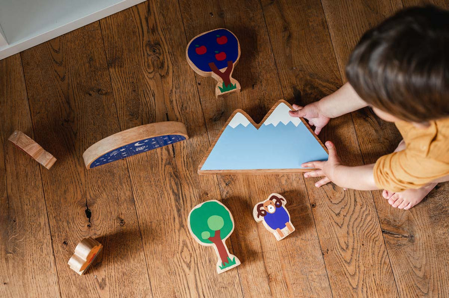 Looking down at a child playing with the Lanka Kade Babipur moel mountain toy and other dan y ser wooden toys on a wooden floor