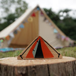 Close up of the Lanka Kade Babipur dan y ser orange tent toy on a log in front of a large beige tent