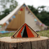 Close up of the Lanka Kade Babipur dan y ser orange tent toy on a log in front of a large beige tent