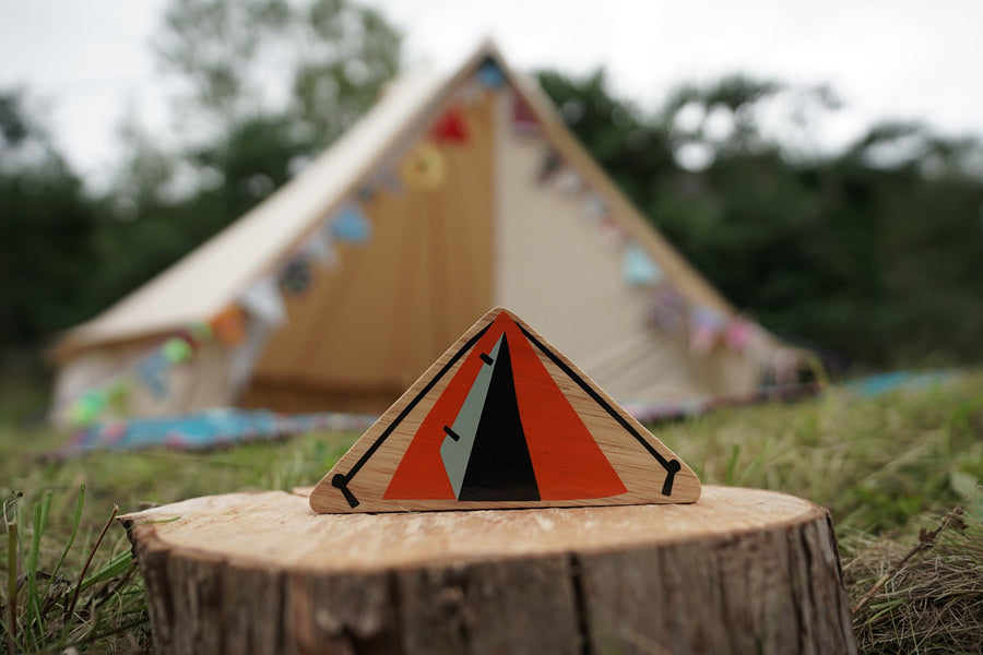 Close up of the Lanka Kade Babipur dan y ser orange tent toy on a log in front of a large beige tent