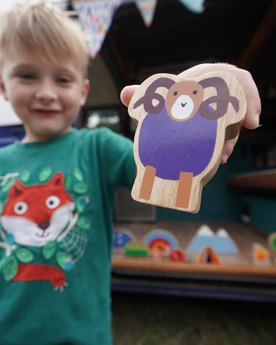 Close up of a boy holding up the Lanka Kade Babipur purple ram wooden toy figure