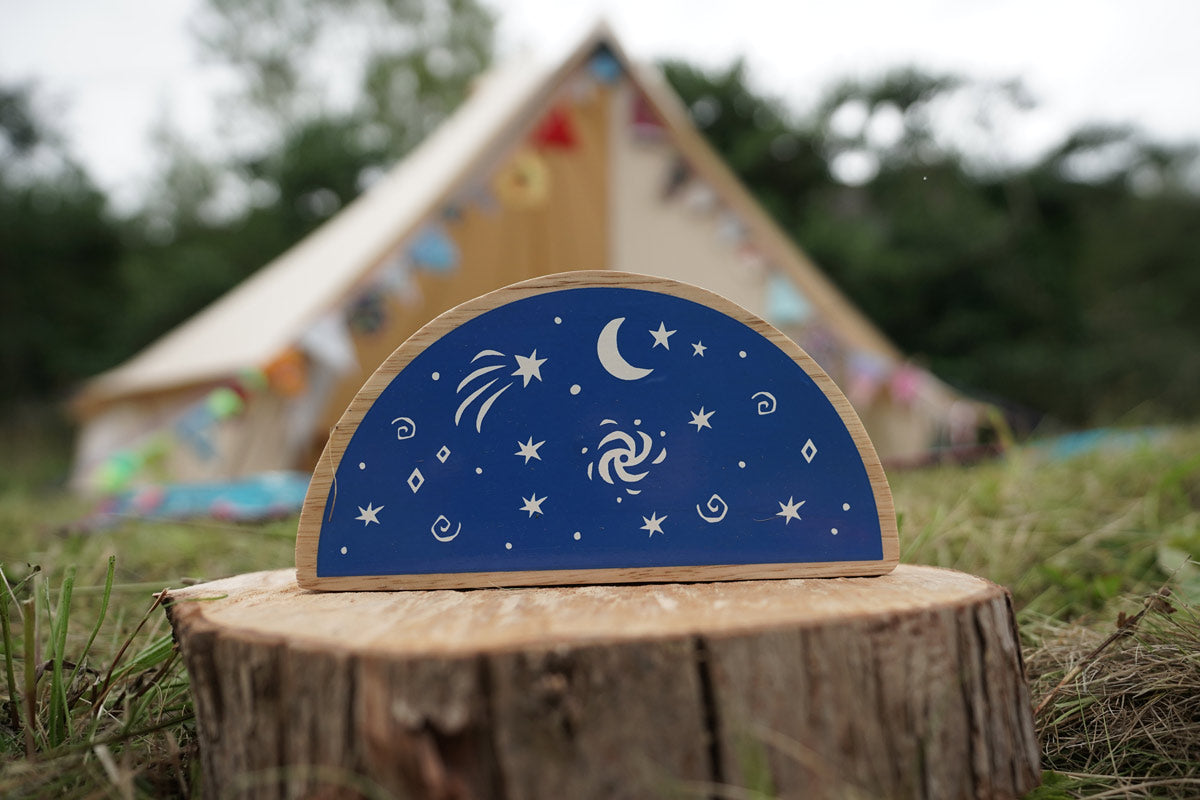 Close up of the Lanka Kade Babipur dan y ser semi circle block toy on a wooden log in front of a beige tent