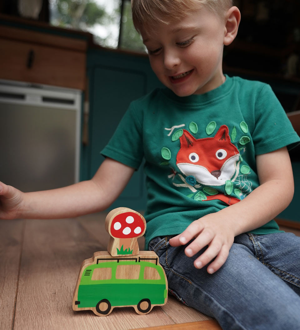 Boy sat playing with the Lanka Kade Babipur lola campervan wooden toy on a wooden surface