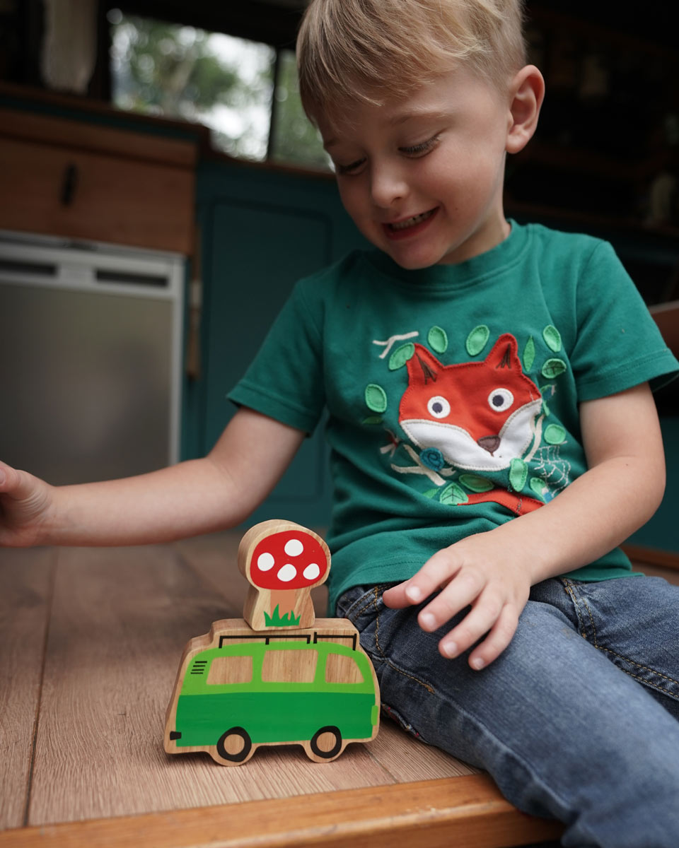 Boy sat playing with the Lanka Kade Babipur lola campervan wooden toy on a wooden surface