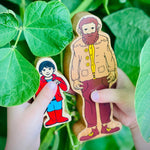 Close up of a child holding the Lanka kade wooden person next to a mystical creatures giant figure in some green leaves