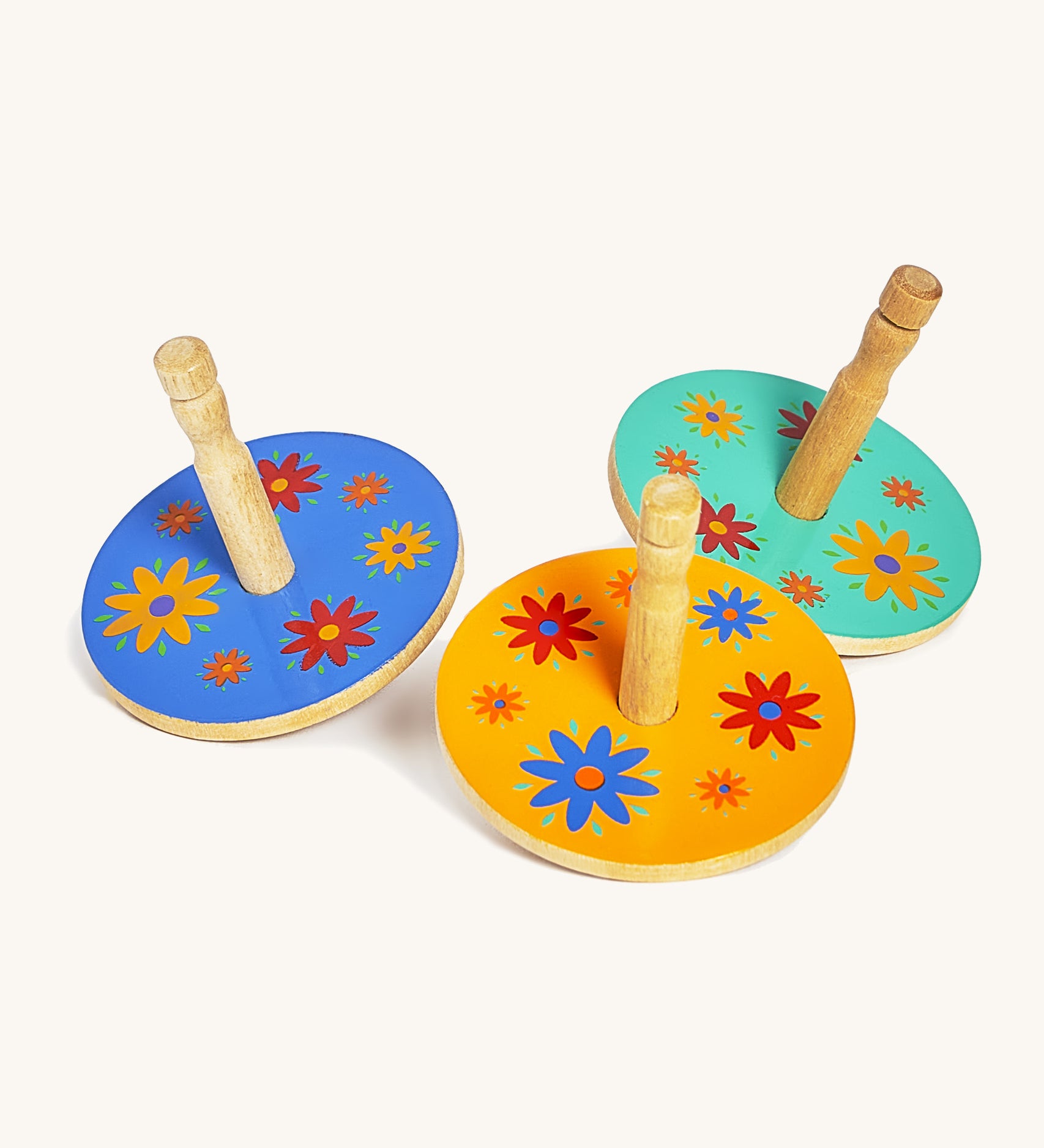 A blue, yellow and green wooden Lanka Kade spinning top next to each other on a cream background.