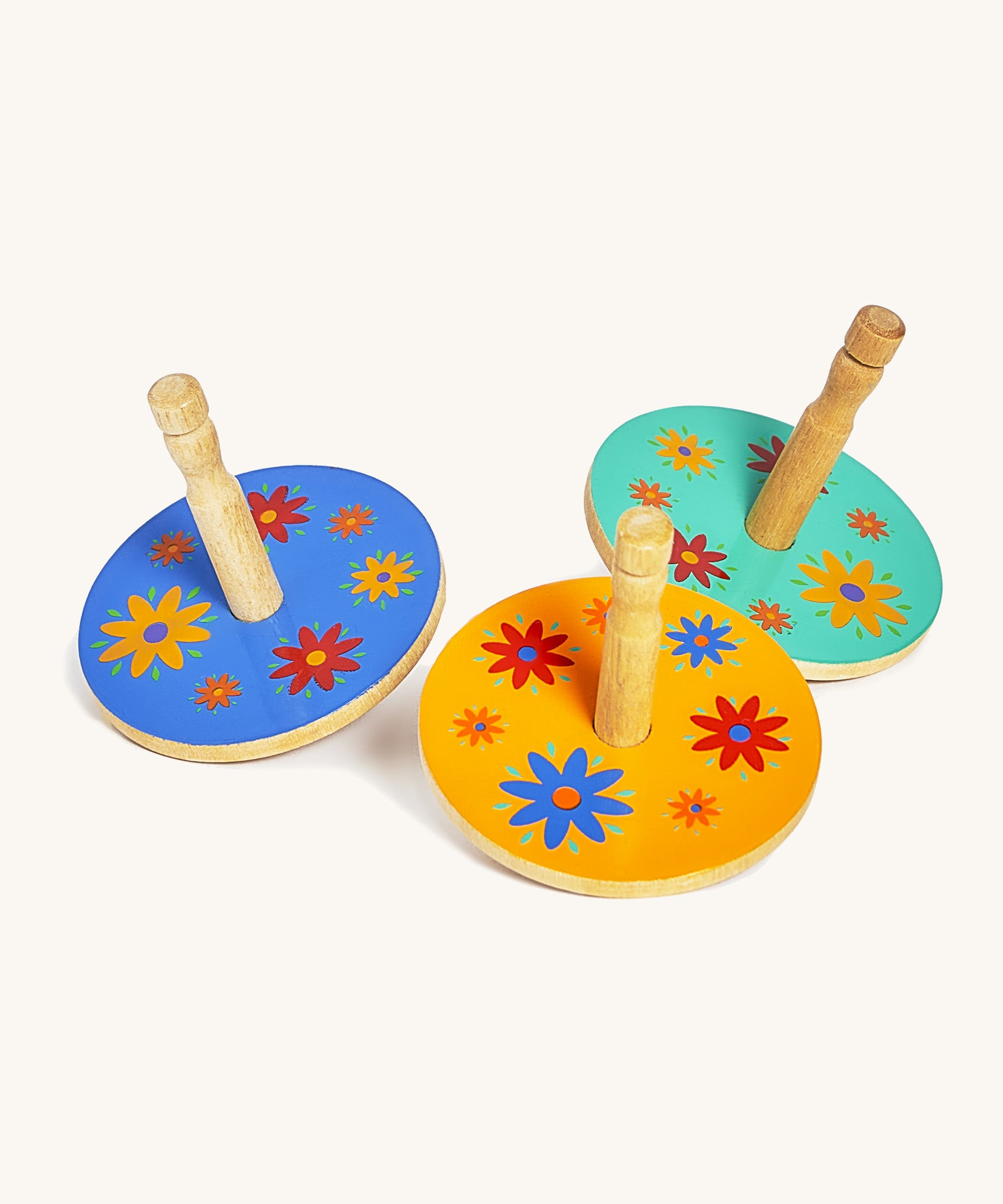 A blue, yellow and green wooden Lanka Kade spinning top next to each other on a cream background.