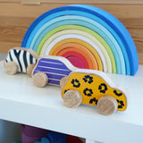 Lanka Kade wooden animal printed cars next to a Grimms rainbow on a shelf. Features a leopard, snail and zebra printed wooden car. 