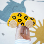 Lanka Lade leopard wooden car. A wooden car with a leopard print in a adult hand holding above a play rug. 