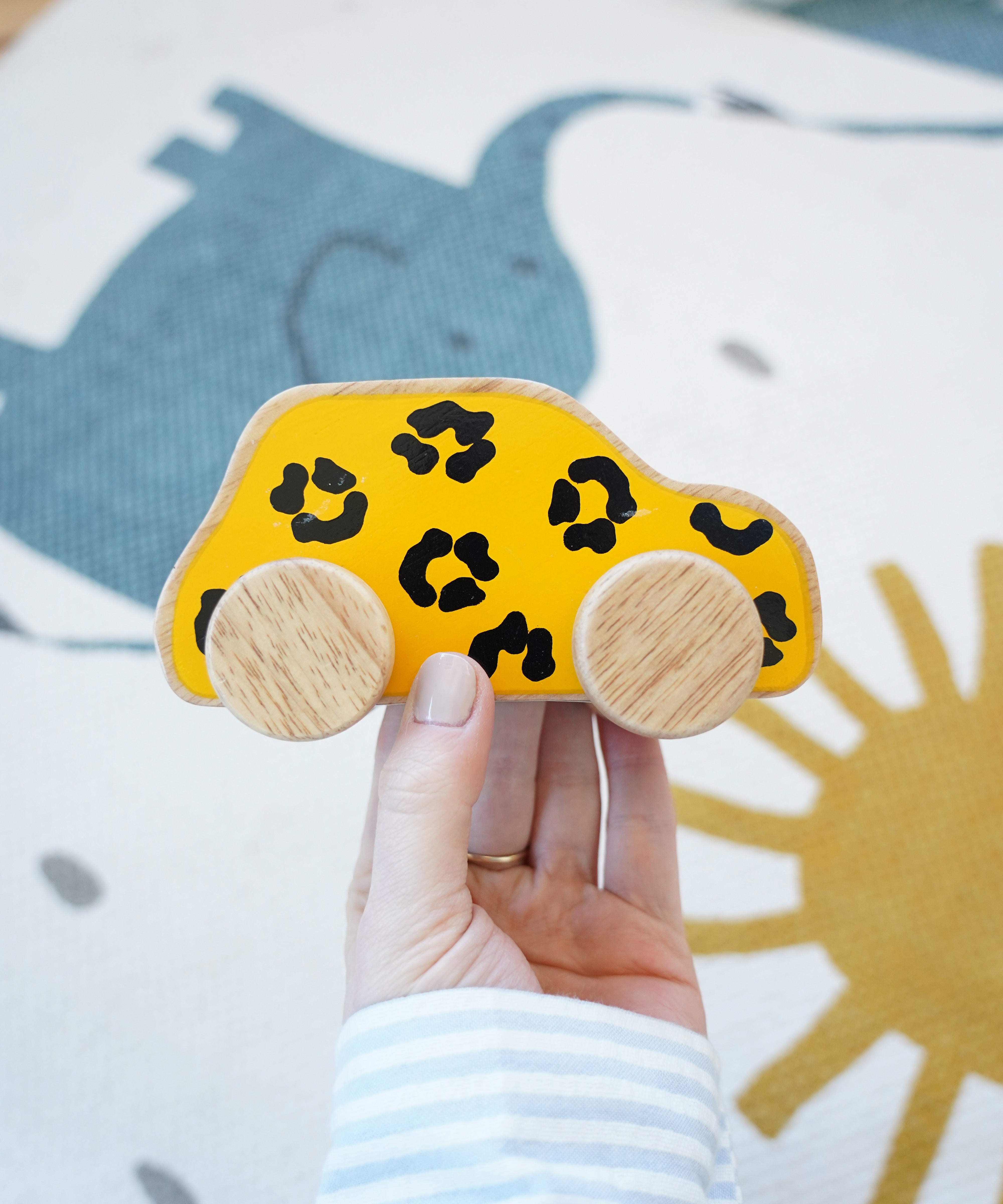 Lanka Lade leopard wooden car. A wooden car with a leopard print in a adult hand holding above a play rug. 