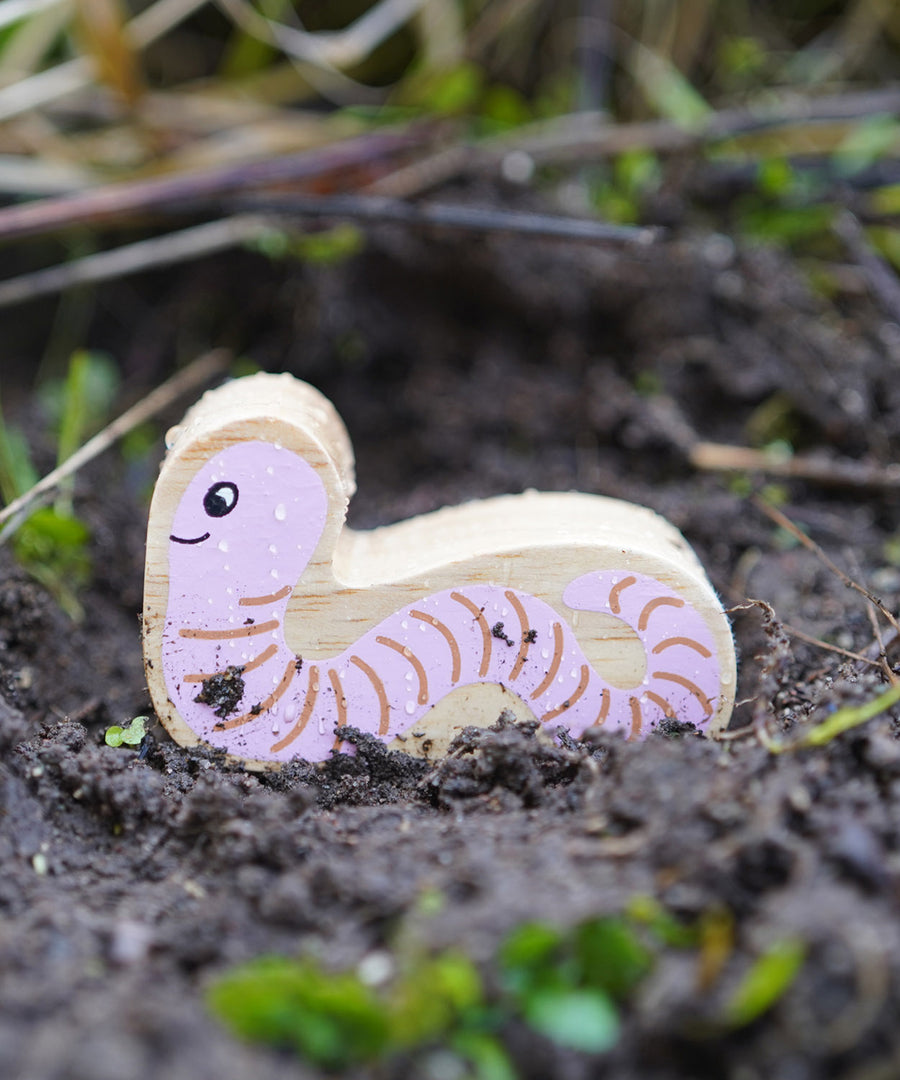 Lanka Kade Wooden Worm Toy is having an adventure outside in the soil!  The worm had a pink with brown lines on its body and a smiling face