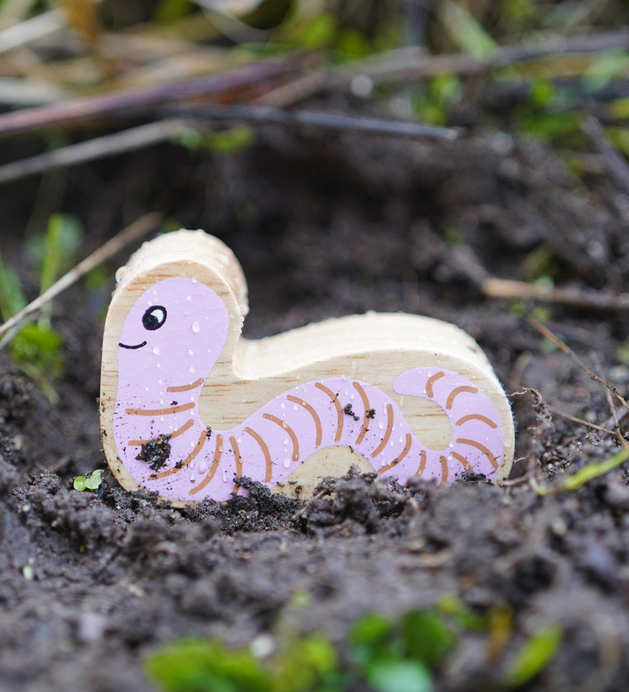 Lanka Kade Wooden Worm Toy is having an adventure outside in the soil!  The worm had a pink with brown lines on its body and a smiling face