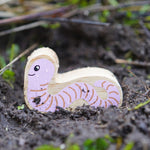 Lanka Kade Wooden Worm Toy is having an adventure outside in the soil!  The worm had a pink with brown lines on its body and a smiling face