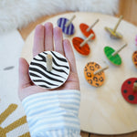 Lanka Kade zebra spinning top in a adult hand above other animal Lanka Kade wooden animal spinning tops on a wooden floor