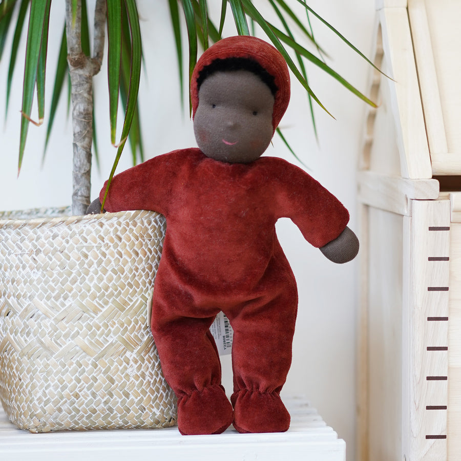 Senger Large Poppy Flower Doll. A velvety red/dark orange natural cloth doll, with a neutral smiling face, dark brown hair poking out from the hood, and a soft body, on a cream background.