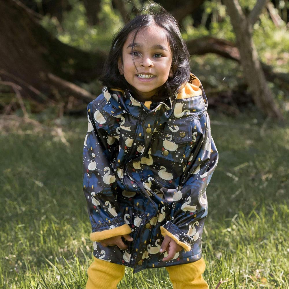 Girl stood in a grass field wearing the Little green radicals night swimming childrens recycled plastic rain coat