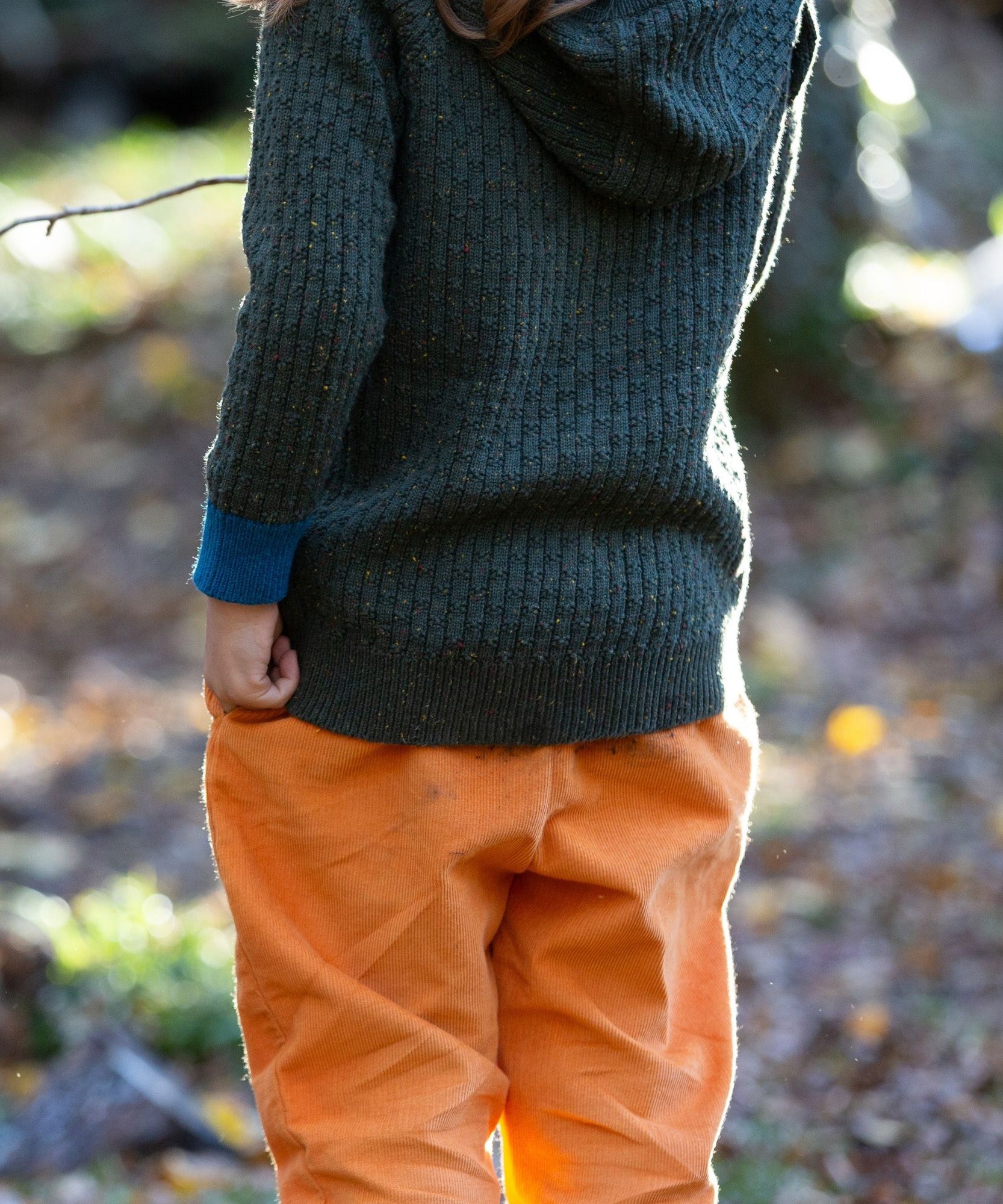 Little Green Radicals kids fern green knitted hooded cardigan with yellow and red pockets worn by a child hem detail