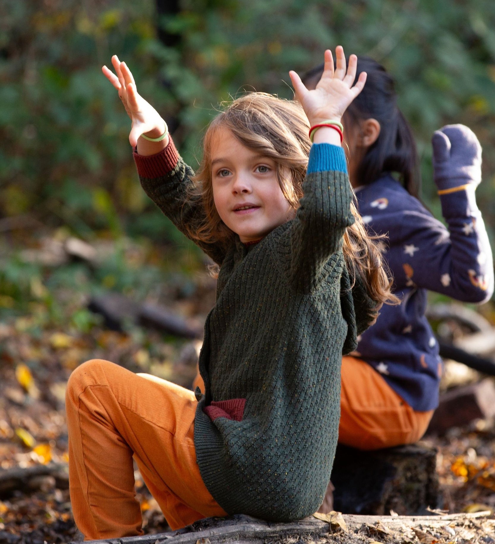 Little Green Radicals kids fern green knitted hooded cardigan with yellow and red pockets worn by a child