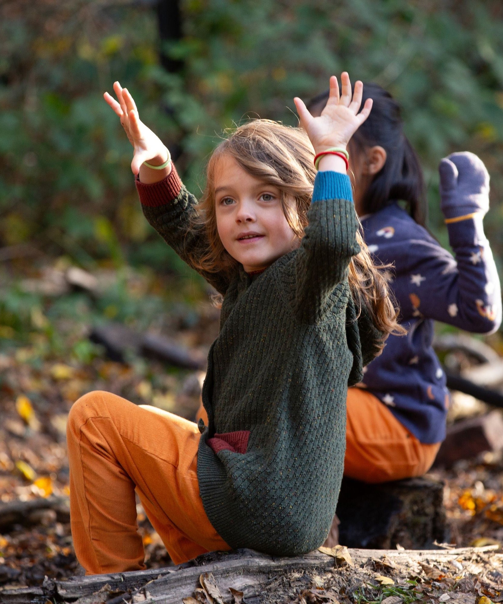 Little Green Radicals kids fern green knitted hooded cardigan with yellow and red pockets worn by a child