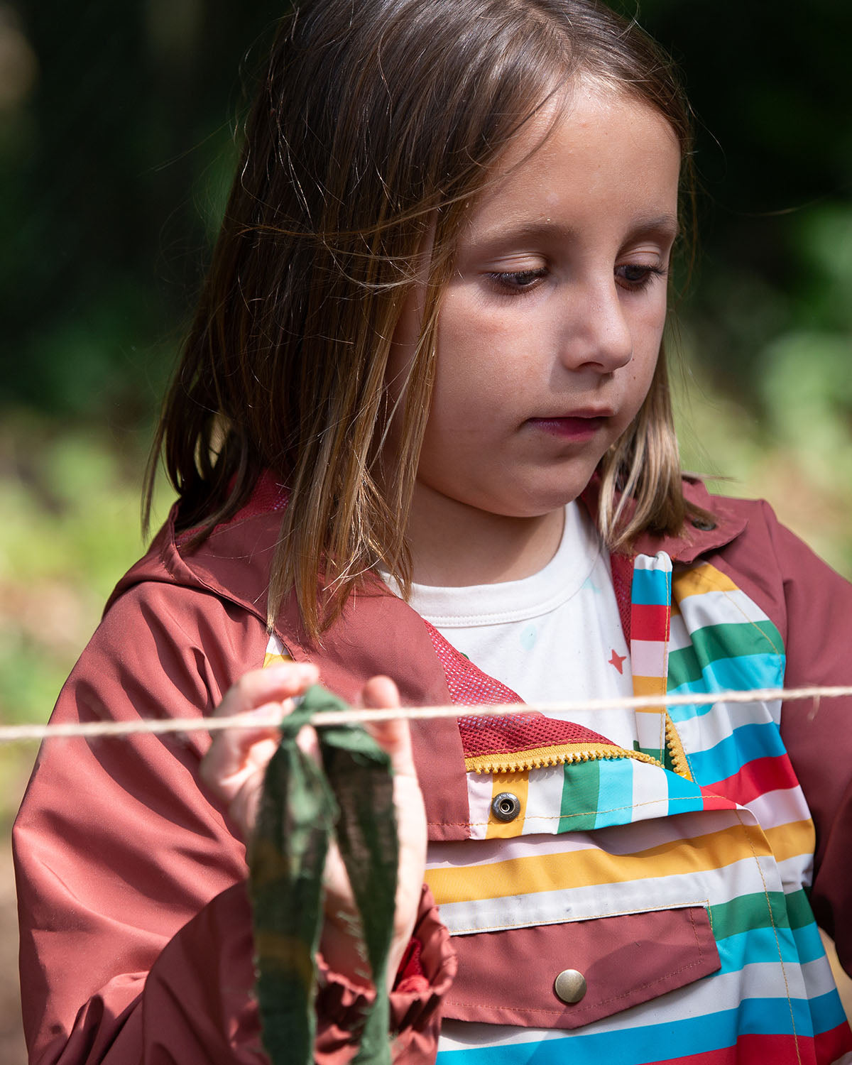 A closer look at the side of the Little Green Radicals Rainbow Striped Recycled Waterproof Windbreaker Jacket on a child