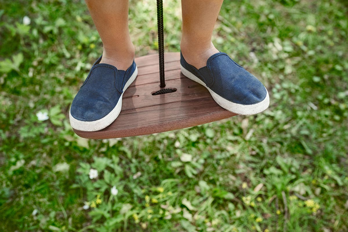 Close up of a boys shoes stood on the Lillagunga walnut wood disco swing