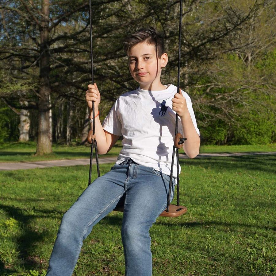 Boy sat on a Lillgunga classic walnut wooden rope swing in a park