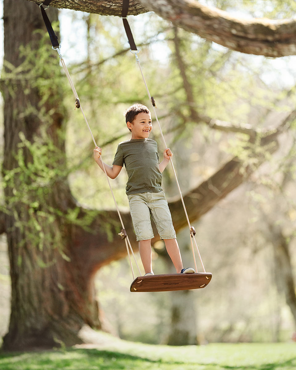 Boy stood on the Lillagunga walnut grand swing hanging from a large tree in a park