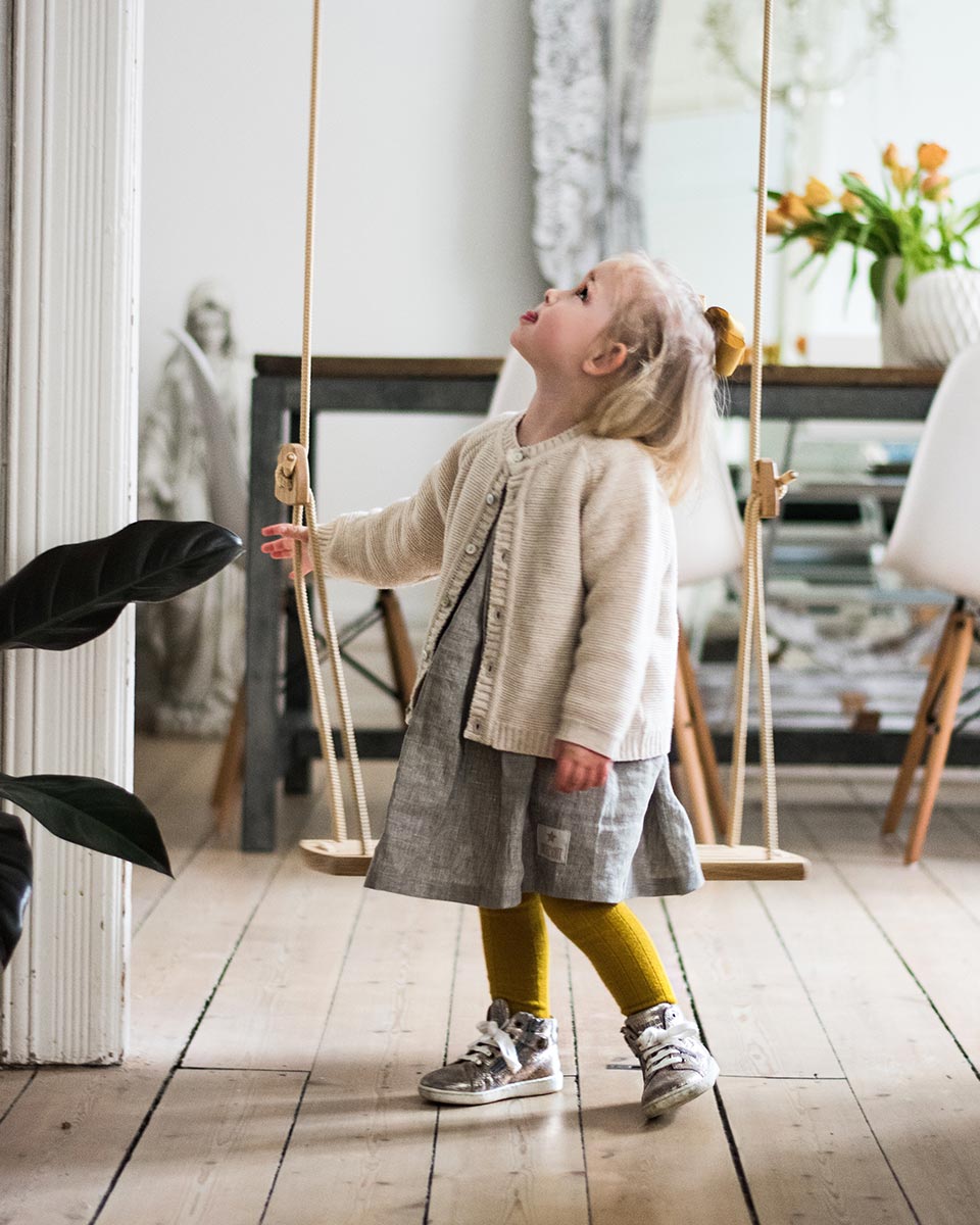 Girl stood looking up at the Lillagunda oak wood grand swing  in a wooden living room