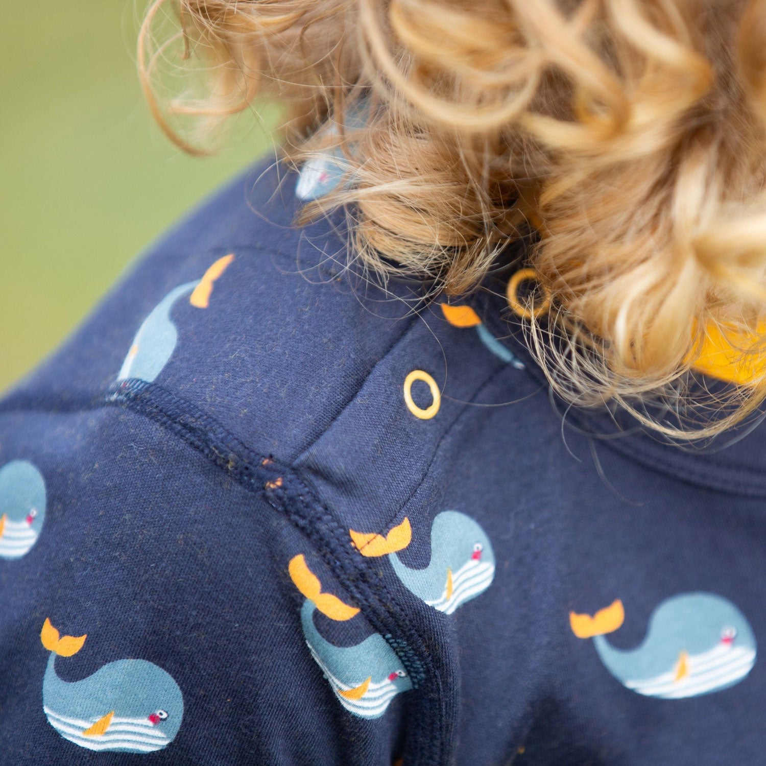 Child wearing the Little Green Radicals Adaptive Easy Feeding Whale Song T-Shirt showing a close up of the popper closure