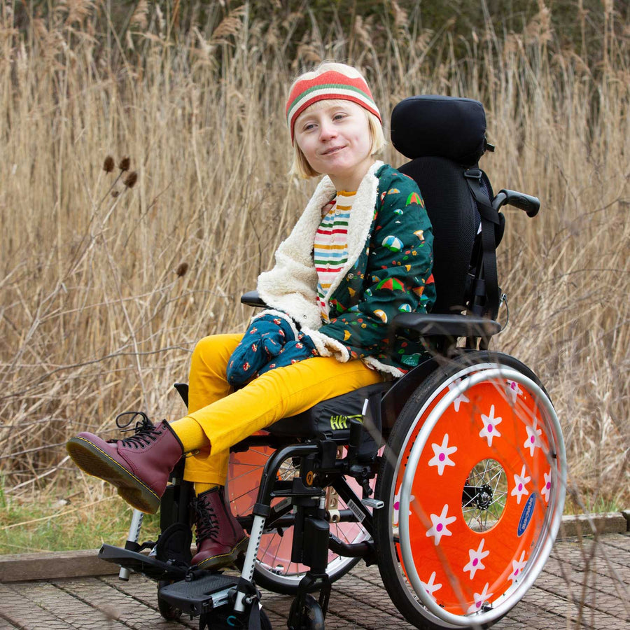 Child wearing the close up of the stripes on the LGR Adaptive Easy Feeding Rainbow Striped Henley Tunic with a LGR sherpa jacket and knitted crown and yellow trousers