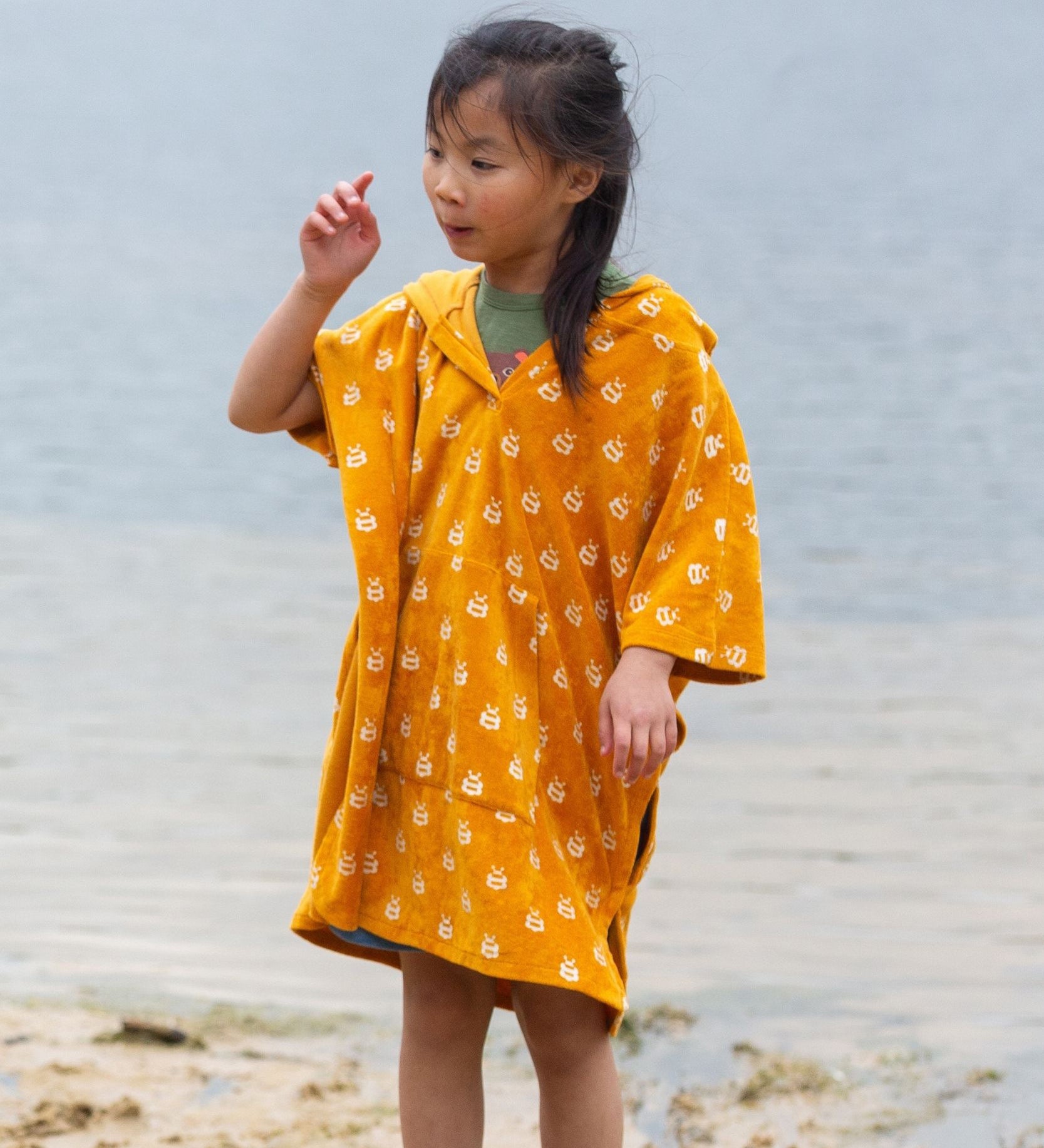 A child wearing the Little Green Radicals Children's Bees patteren Hooded organic cotton Beach Towel Poncho