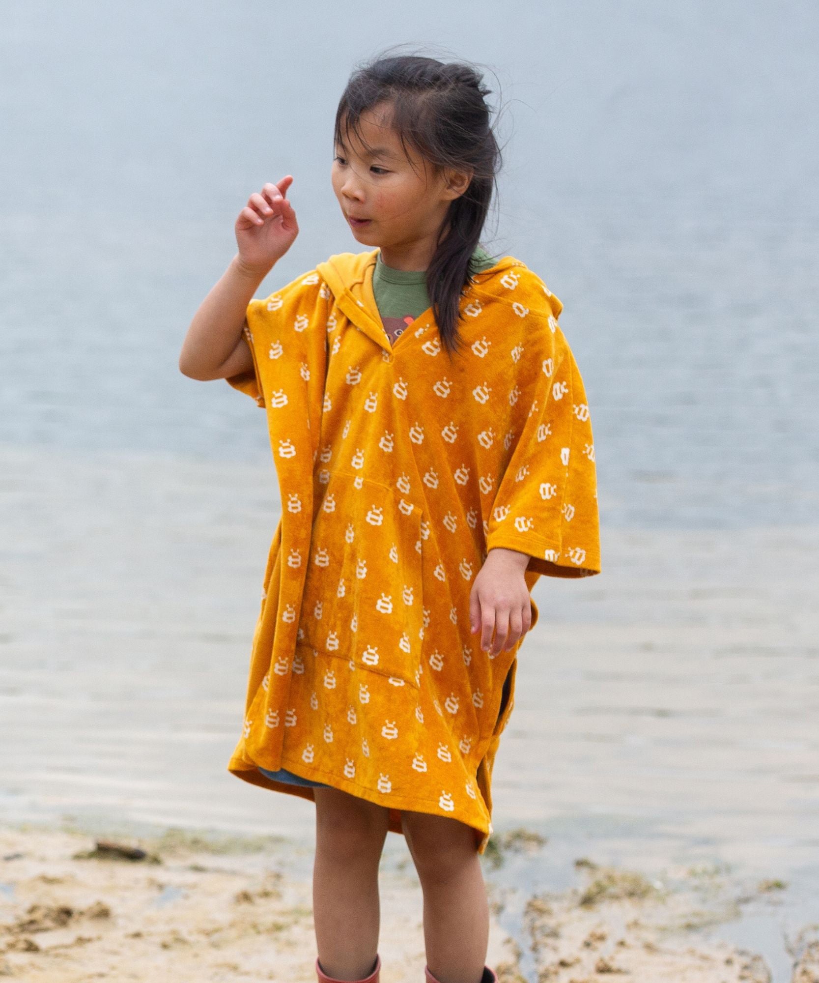 A child wearing the Little Green Radicals Children's Bees patteren Hooded organic cotton Beach Towel Poncho