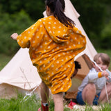 A child wearing the Little Green Radicals Children's Bees pattern Hooded organic cotton Beach Towel Poncho, facing away from the camers.