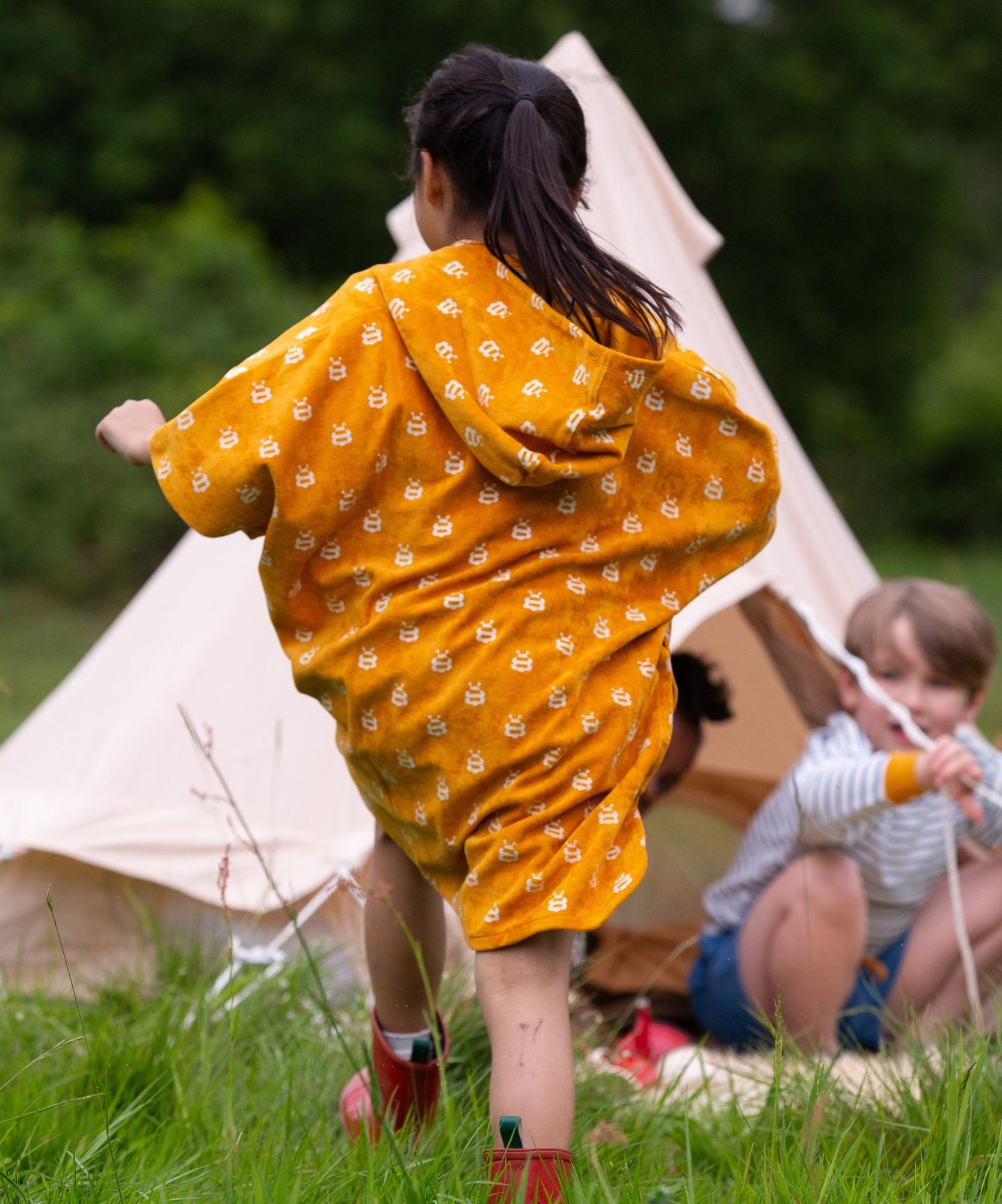 A child wearing the Little Green Radicals Children's Bees pattern Hooded organic cotton Beach Towel Poncho, facing away from the camers.