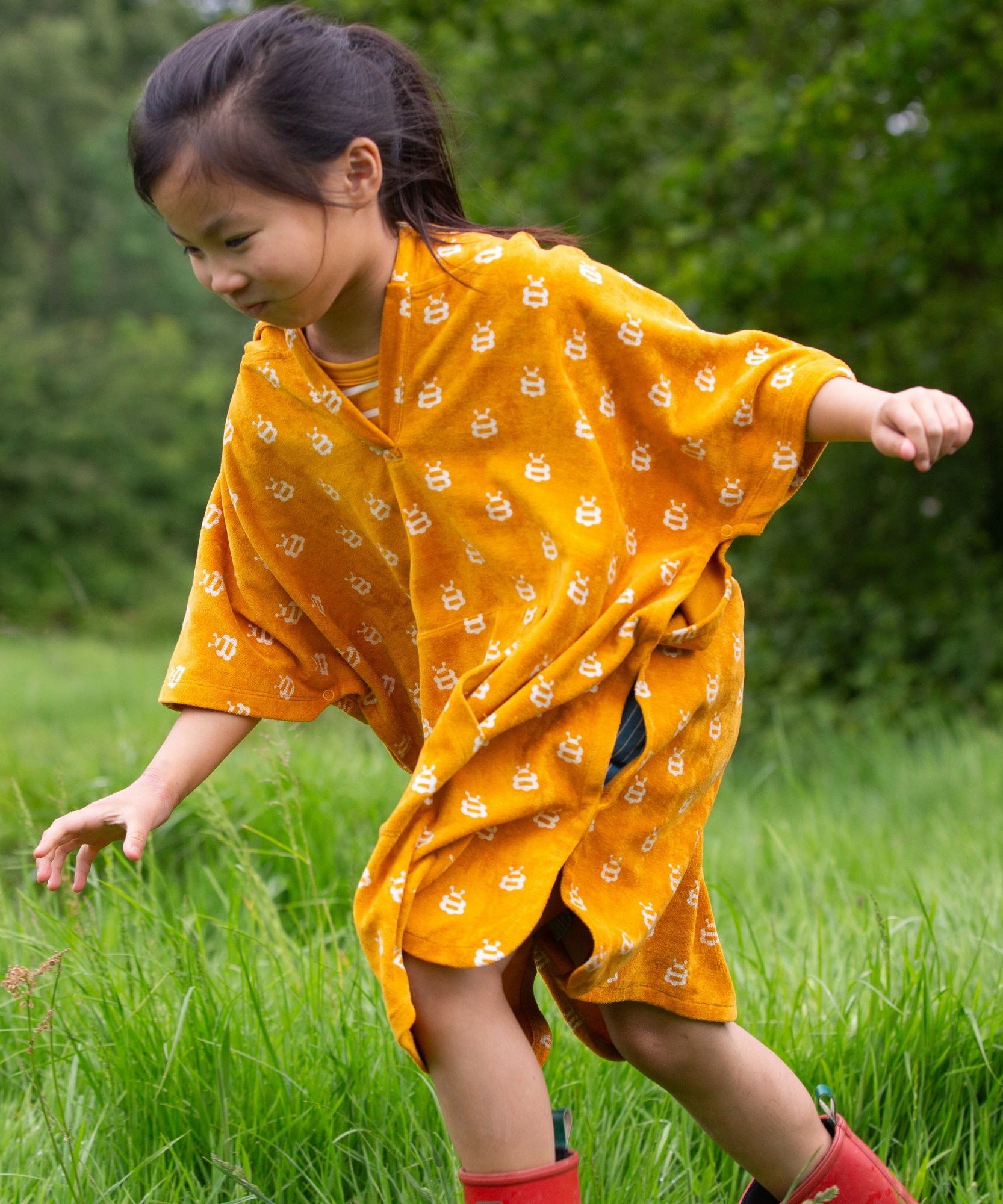 A child wearing the Little Green Radicals Children's Bees pattern Hooded organic cotton Beach Towel Poncho