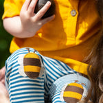 A close up of a child's knees wearing the Little Green Radicals Bees Knees Patch Striped blue and white Joggers. The bee appliques can be seen closely. 