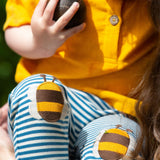 A close up of a child's knees wearing the Little Green Radicals Bees Knees Patch Striped blue and white Joggers. The bee appliques can be seen closely. 