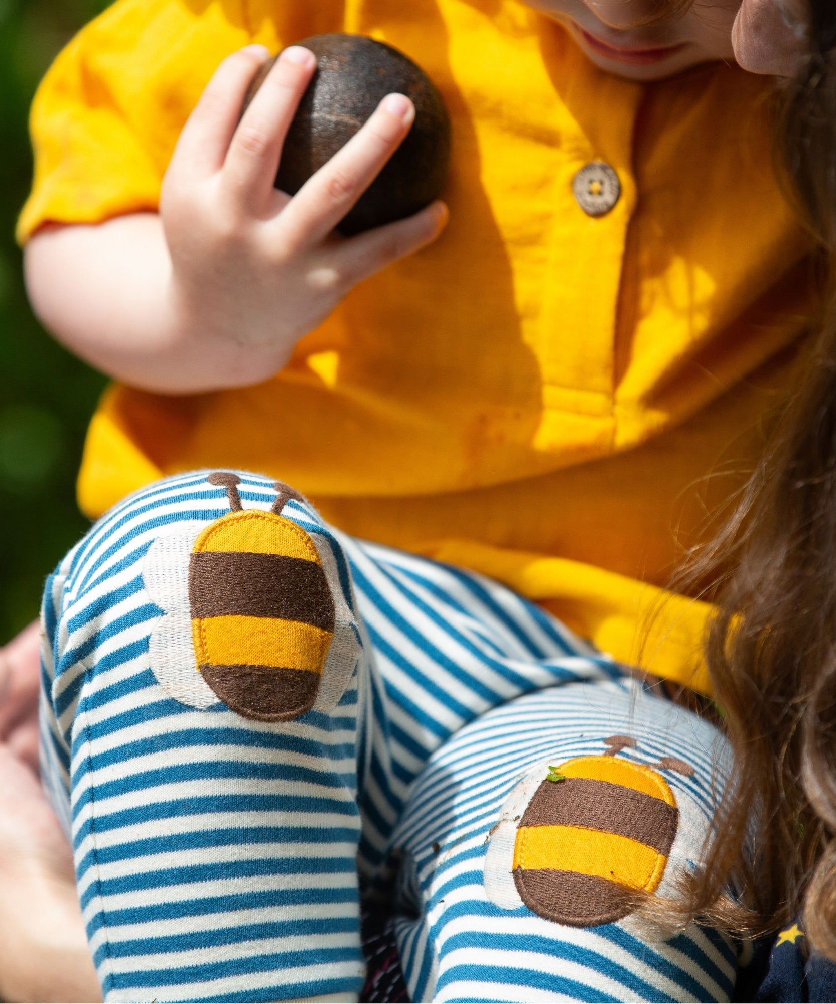 A close up of a child's knees wearing the Little Green Radicals Bees Knees Patch Striped blue and white Joggers. The bee appliques can be seen closely. 