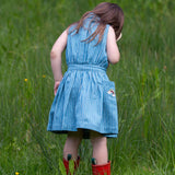 A child wearing the Little Green Radicals Child's Organic Cotton Horizon Blue Striped Pinafore Button Dress with red wellington boots. 