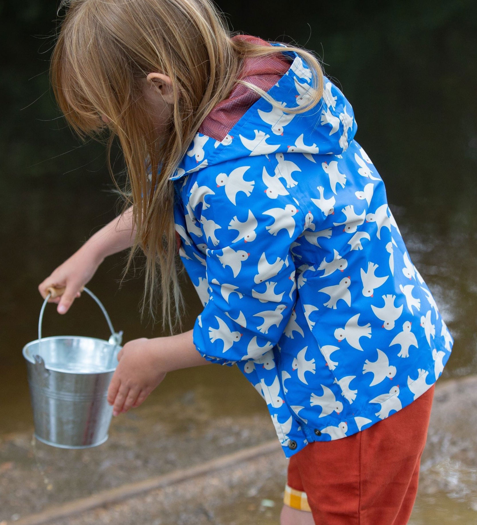 A side view of a child wearing the Little Green Radicals Diving And Splashing Blue Recycled Waterproof Kids Packable Anorak