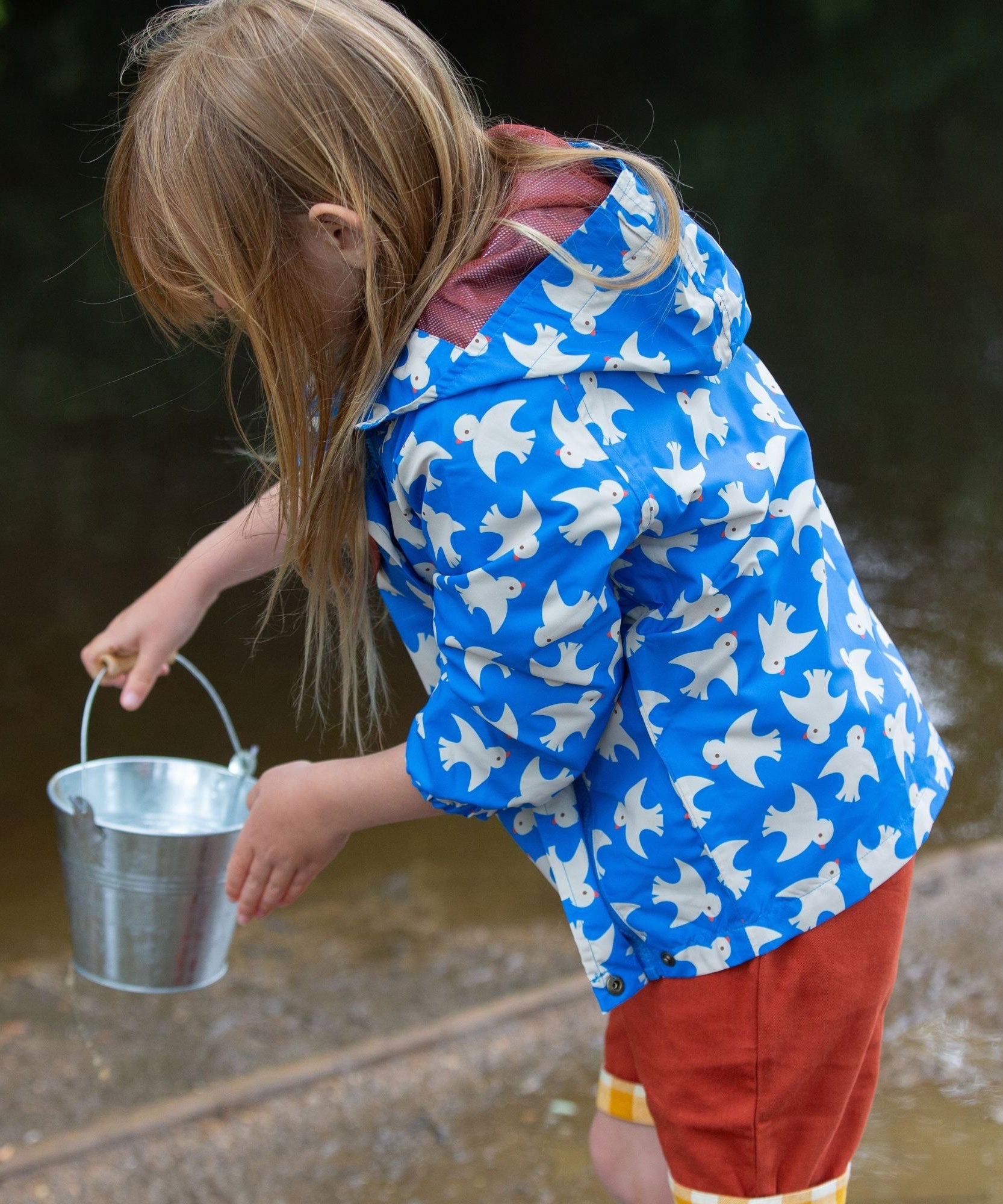 A side view of a child wearing the Little Green Radicals Diving And Splashing Blue Recycled Waterproof Kids Packable Anorak