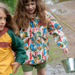 A child wearing the Little Green Radicals Child's Flora & Fauna vintage style flower print Waterproof Raincoat. Another child can be seen to the side of them.