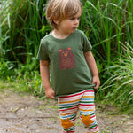 A child wearing the Little Green Radicals Kids Organic Cotton Green Bear Short Sleeve T-Shirt with rainbow striped star knee patch joggers.