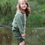 A child wearing the Little Green Radicals From One To Another Olive Green Striped Knitted Child's Organic Cotton Cardigan with green coloured shorts.